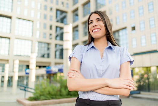 Young beautiful business woman standing in front of office building and smile looking into the distance.
