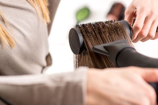 Close-up of a drying brown hair with hair dryer and round brush. 