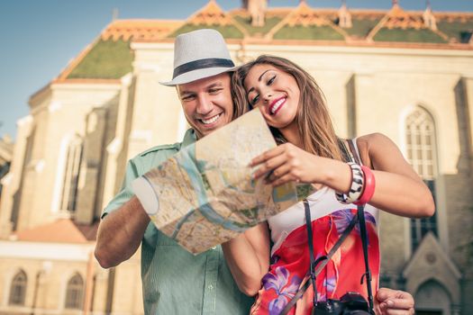 Happy couple of tourists on vacation studying map of city