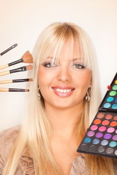 Beautiful young woman with brilliant smile holding an eyeshadow colour and make up brushes