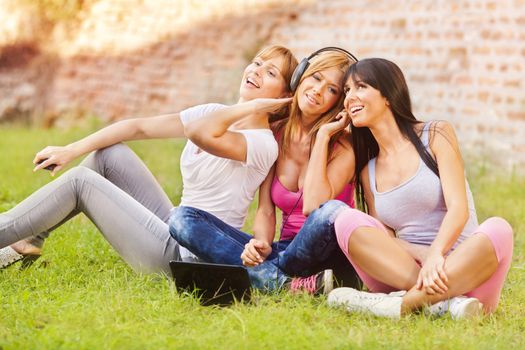 Three young beautiful girls listen music from notebook, outdoor