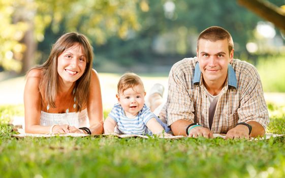Beautiful happy family lie on the grass in park