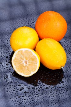 Juicy delicious oranges and lemons on reflective table with water drops