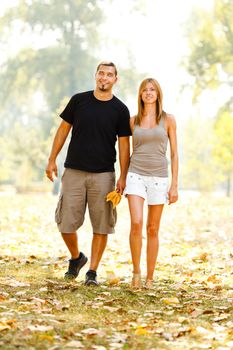 Beautiful happy couple holding hands and walking through the park