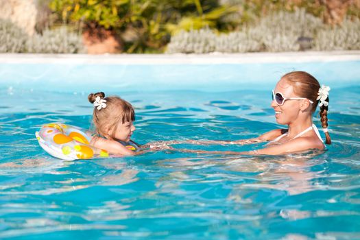 Happy little girl swimming in the pool with mother