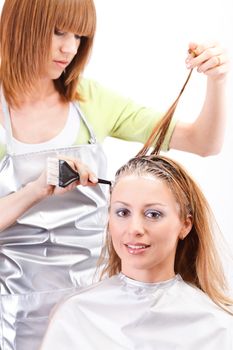 Young beautiful hairdresser coloring hair with hair color