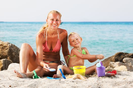 Happy little girl with mother on the beach with bucket and spade