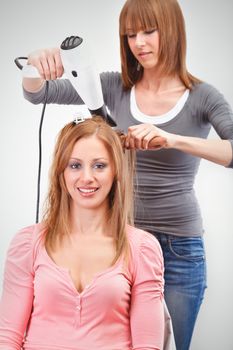 Beautiful young hairdresser drying woman hair