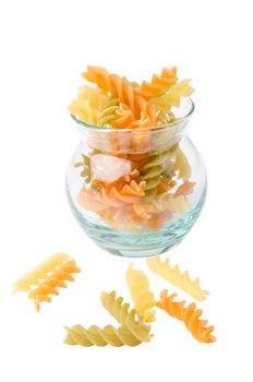 Uncooked italian pasta - three colors spirals in glass cup on white background.