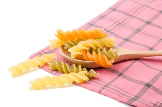 Uncooked italian pasta - three colors spirals in wooden spoon on tablecloth.