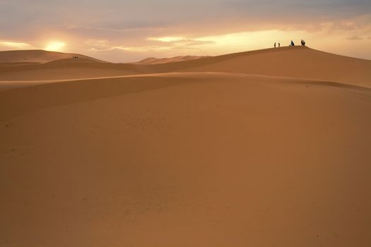 People standing on a sand dune, silhouetted against the sunset, Sahara Desert, Morocco