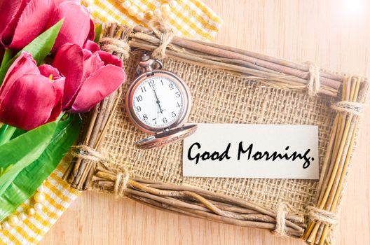 Good morning paper tag in sack photo frame and vintage alarm clock with red tulip on wooden background.