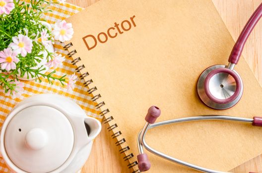 Stethoscope With Note Book with flower on wood background.