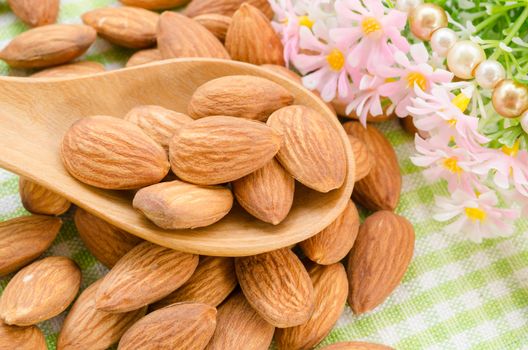 Almonds in wooden spoon with flower on tablecloth.