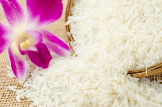 Raw rice with violet orchid flower in weave basket on sack background.