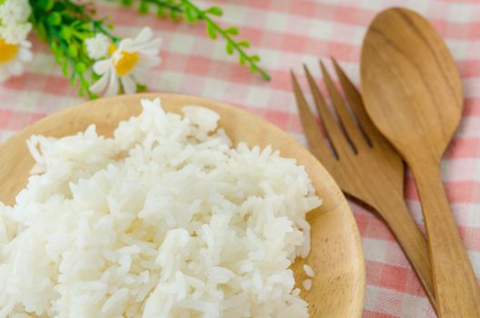 Bowl of Cooked Rice and wooden spoon with flower on tablecloth.