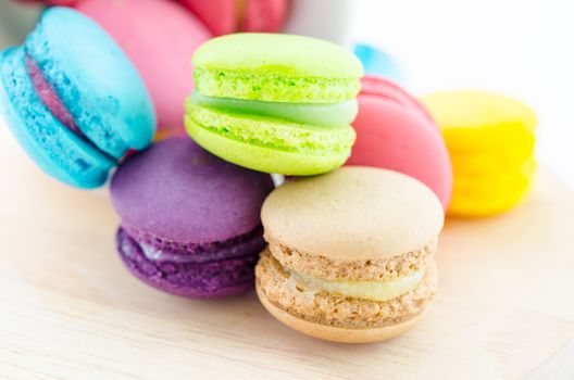 Colorful macaroons in white cup on wooden background.