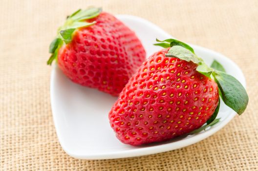 Ripe red strawberries in white cup heart shape on sack background.