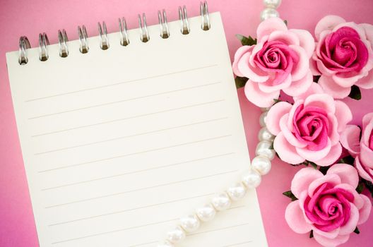 roses and open notebook on pink background.