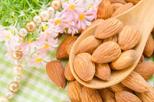 Almonds in wooden spoon with flower on tablecloth.