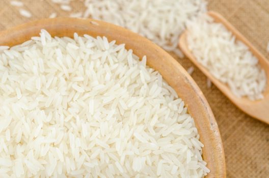 Raw white rice in wooden bowl on sack background.