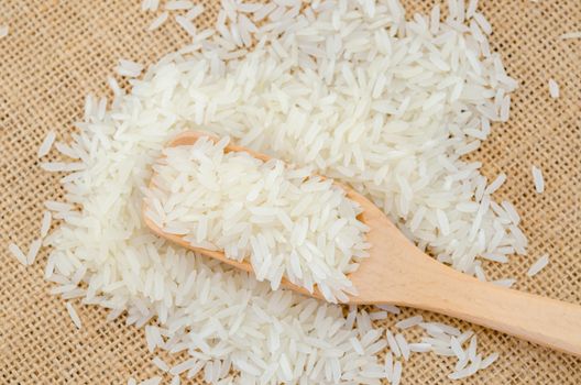 Raw white rice in wooden spoonl on sack background.