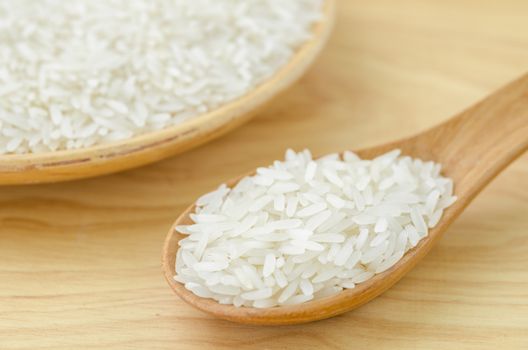 white rice grains with wooden spoon on wooden table
