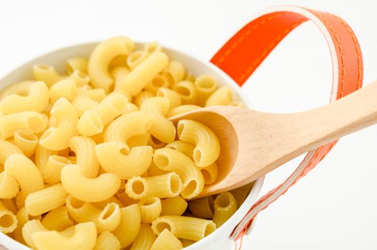 Raw dry elbow macaroni with wooden spoon. Italian Pasta raw food in white bowl on white background.