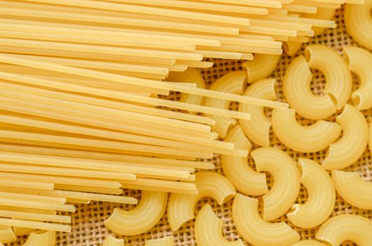 Raw spaghetti and Elbow macaroni noodles on sack background.