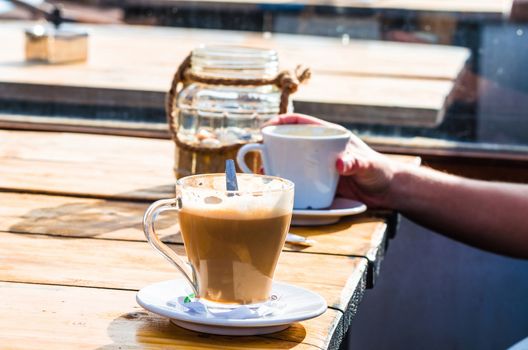 A cup of milk with coffee on the table of a beach bar. Background slightly blurred.
