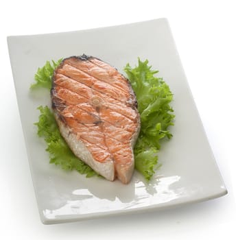 Roasted salmon steak with fresh green lettuce on the white plate