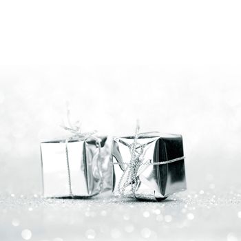 Decorative silver boxes with holiday gifts on shiny glitter background