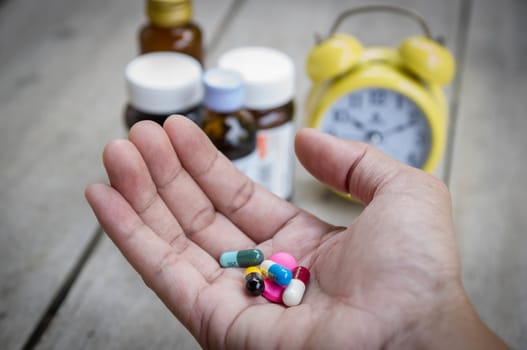 Man's hand hold many medicine, boxes of medicines and clock in the background