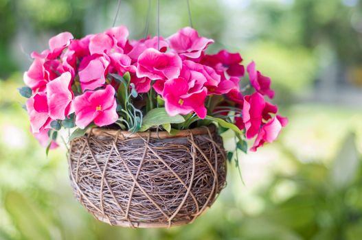 bouquet of artificial flowers in wicker vase on green background.