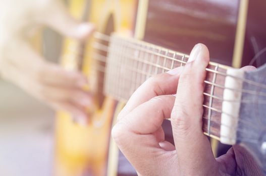 Hand playing acoustic guitar, color filter.