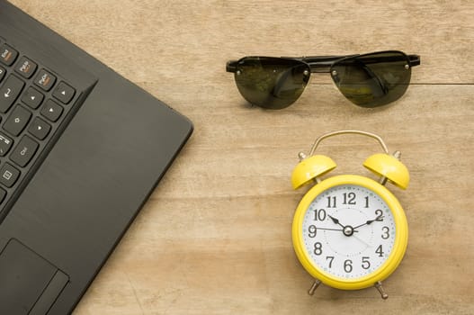 Black notebook  and yellow clock with eye glass on woodenbackground.