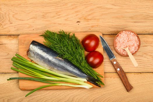 Herring double fillet with onion, dill and tomatoes on bamboo board win small knife, pink salt in wooden scoop on vintage wooden table surface