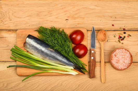 Herring double fillet with onion, dill and tomatoes on bamboo board win small knife, assorted peppercorns, pink salt in wooden scoop on vintage wooden table surface