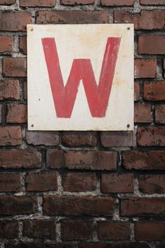 Old sign with letter W on a brick wall.