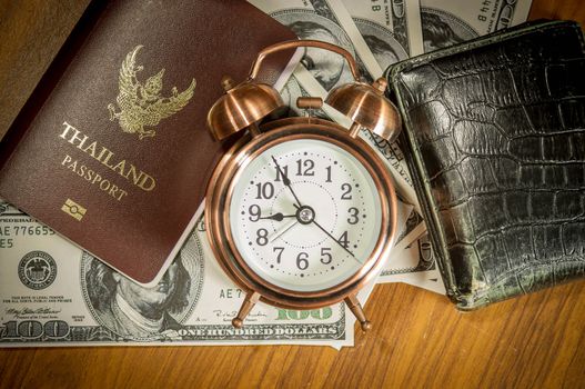 Thailand passport laying atop a pile of American dollars.Clock , wallet.