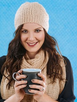 Photo of a beautiful brunette wrapped in warm scarf and hat, drinking a hot coffee, or hot chocolate.