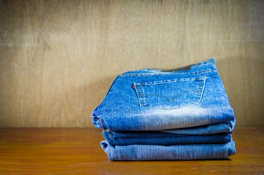 Lot of different old blue jeans on wood background.