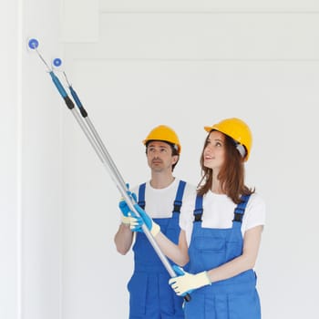 Two workers in helmets painting wall with paint roller