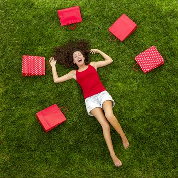 Beautiful and happy young woman lying on the grass surrounded by red gift bags