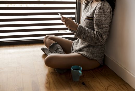 Woman sitting on the floor drinking a coffee and texting