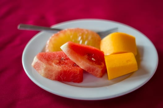 Fresh fruits on disk on red tablecloth.