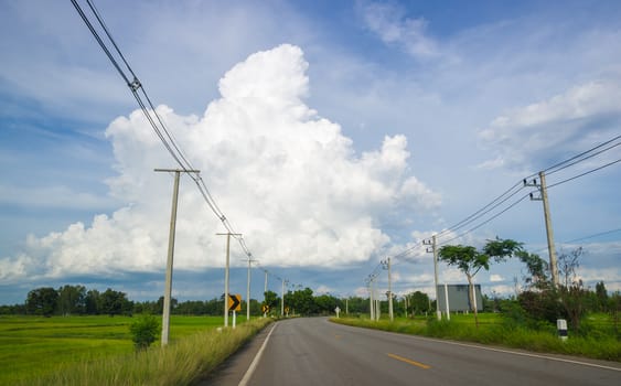 Asphalt road through the green field and clouds on blue sky.