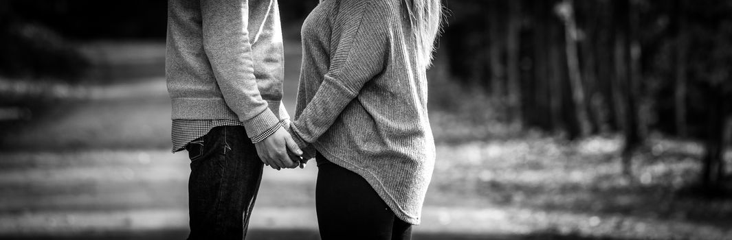 A hopeful young couple holding hands facing each other while stopped during a walk along a country road.