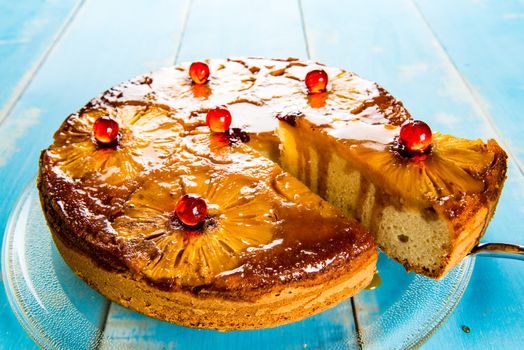 Upside down pineapple cake with caramel. A piece of cake is cut off and the caramel flowing on the side.