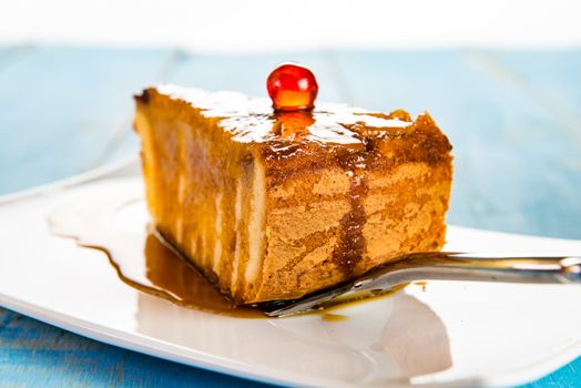 A pice of pineapple cake with caramel on white plate and blue wood table